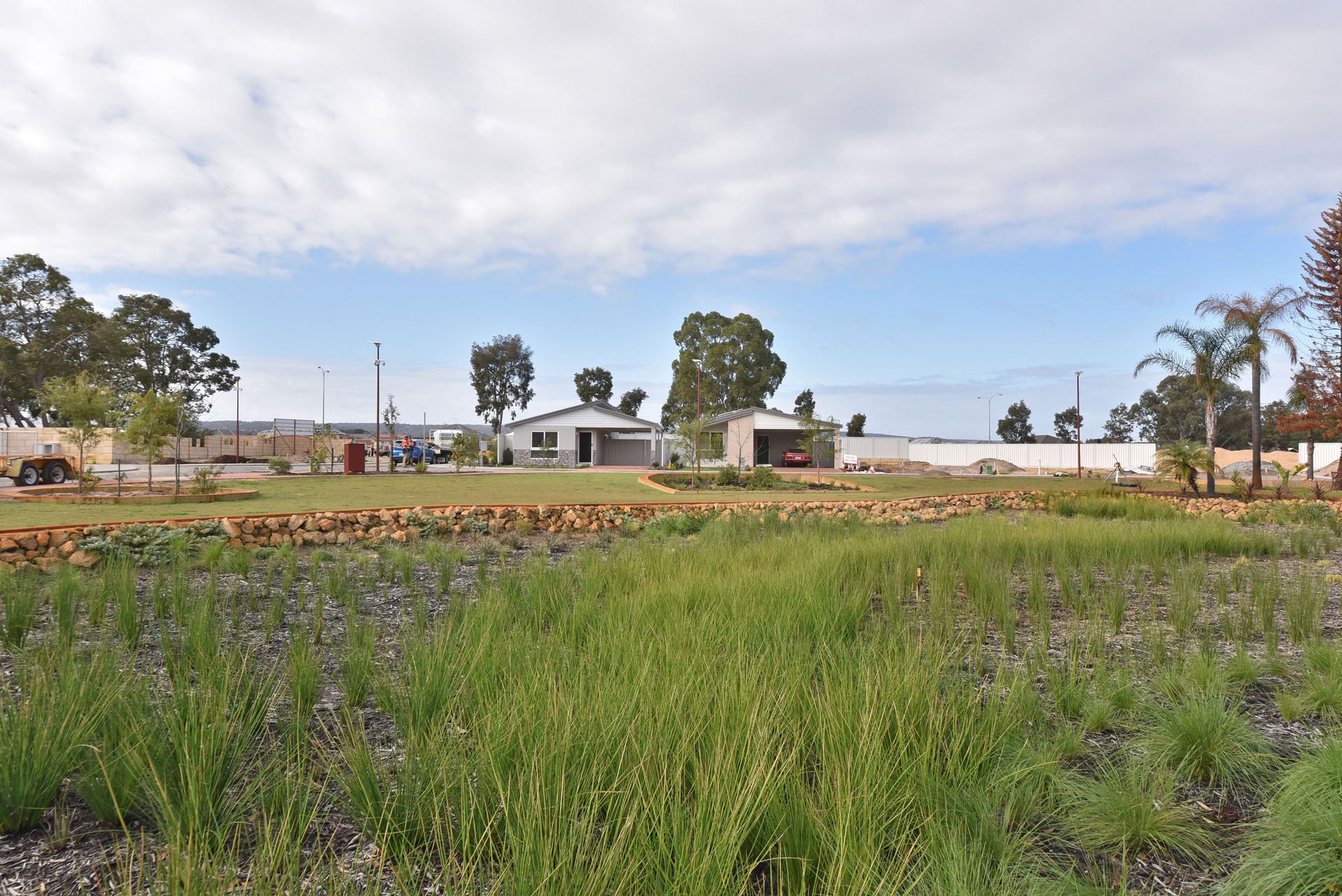 A serene grassy area featuring a prefabricated home surrounded by trees in the Champion Lakes lifestyle village.
