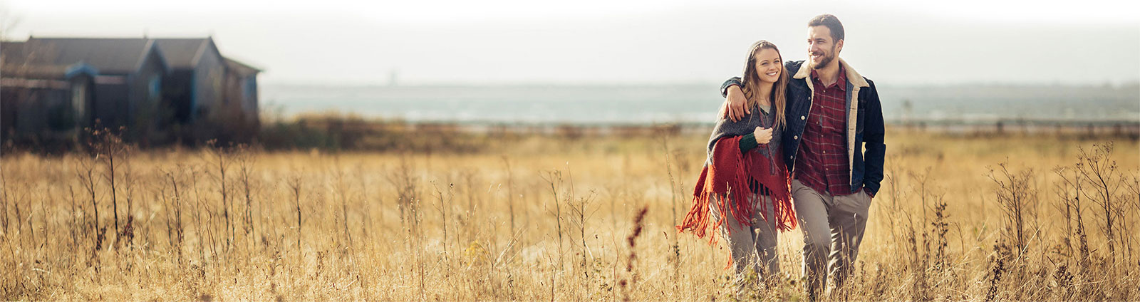 Happy young couple walking in a field of crop whilst looking into the distance of their new home | Evoke Living Homes 